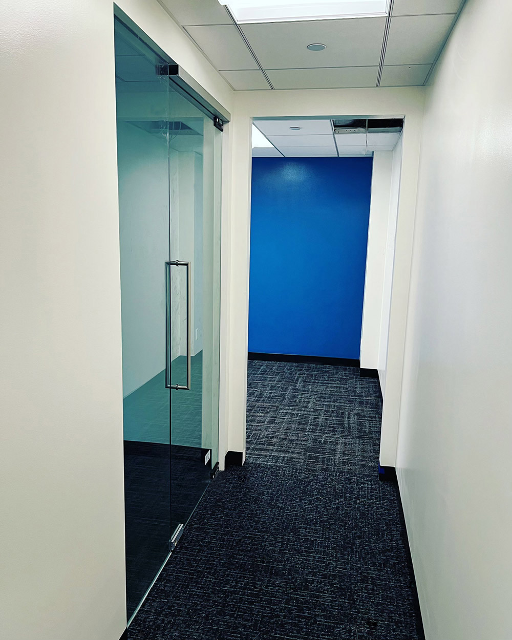Clear glass office partitions and a glass door along an interior corridor