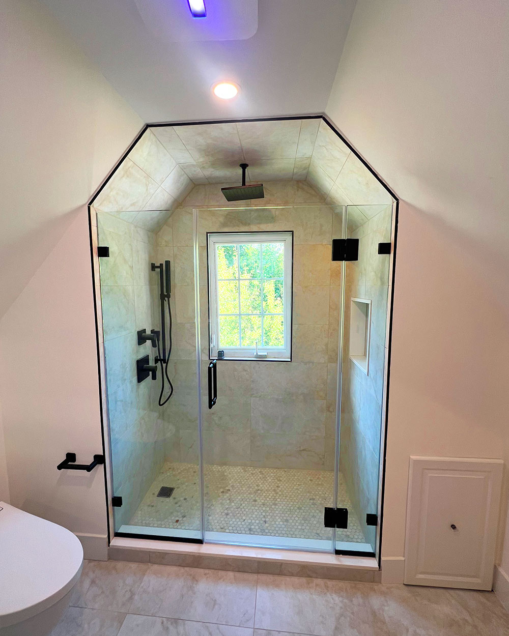Clear shower glass follows the angled ceiling, with a hinged door and black fittings