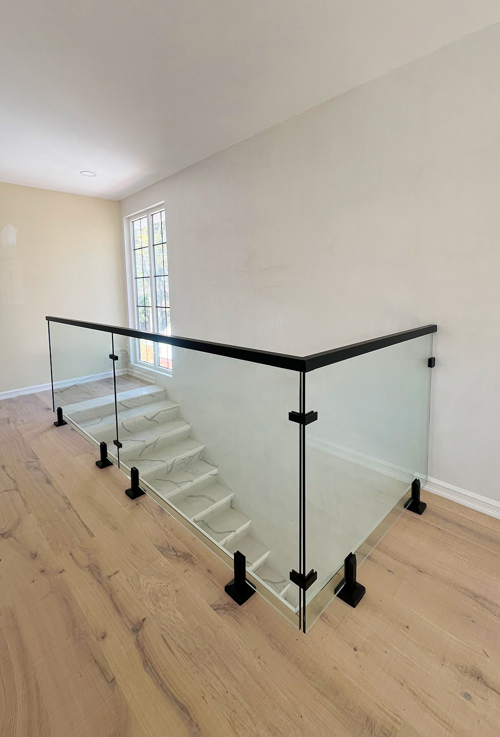 Clear glass railing panels follow a stair opening, with a black top rail and floor brackets