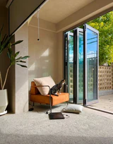 Cat sitting on an ochre chair beside open bi-folding glass doors in a sunlit living space
